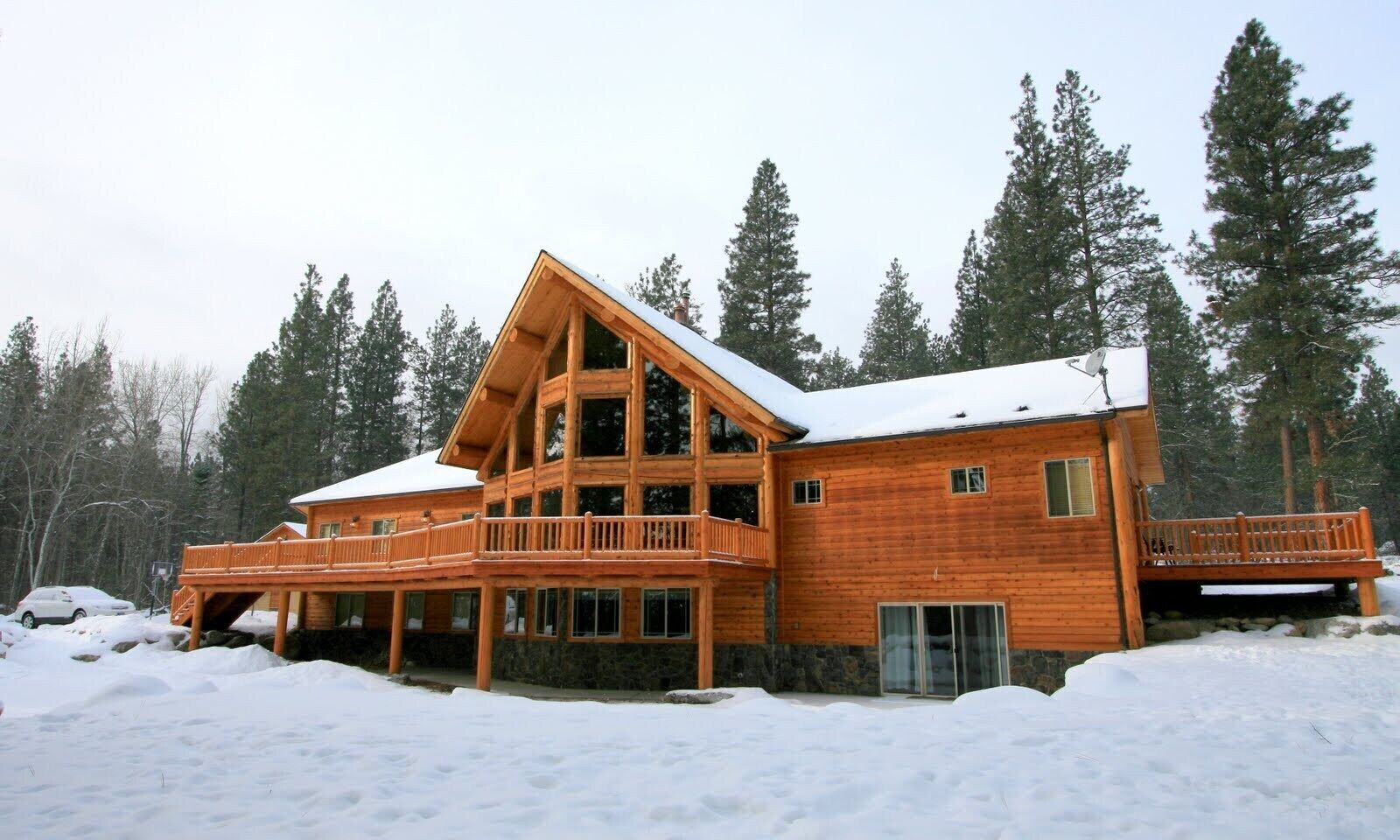 A large wooden cabin with multiple balconies and a covered entrance, surrounded by snow and trees.