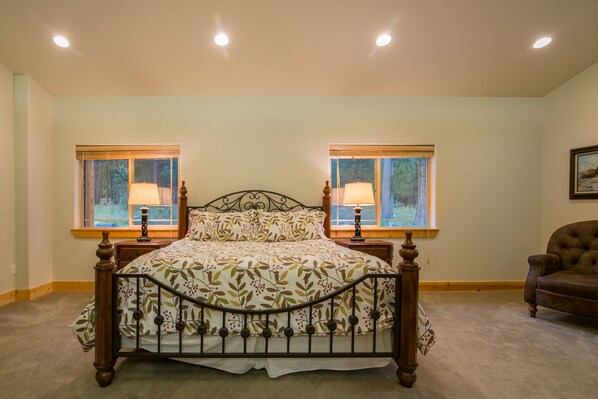 A bedroom with a four-poster bed, two bedside lamps, and two windows with blinds.