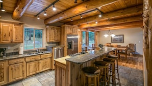 A spacious kitchen with wooden cabinets, a large island with bar stools, stainless steel appliances, and a view of the outdoors. - Pineview Lodge (Hamilton)