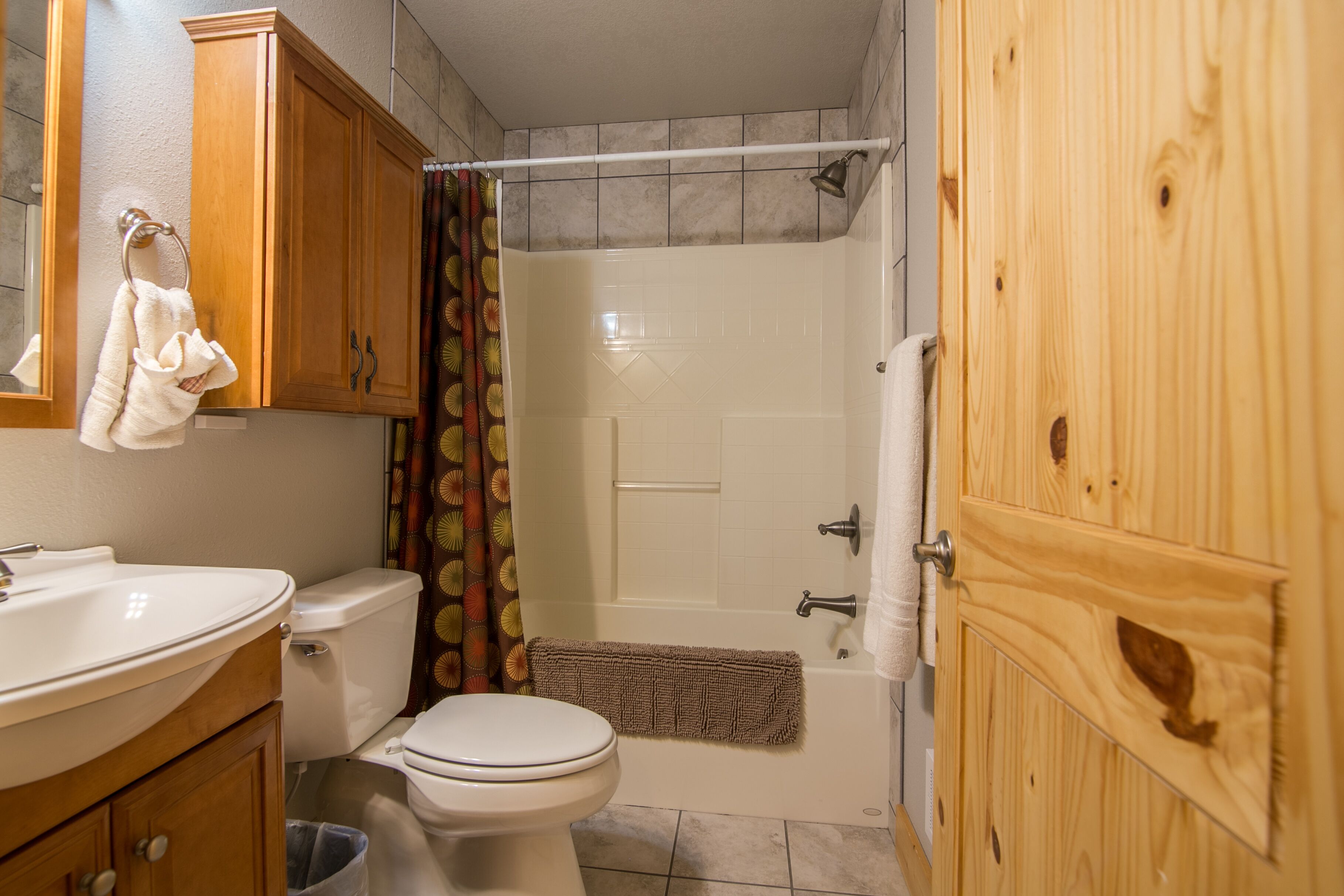 A bathroom with a toilet, sink, shower, and wooden cabinets.