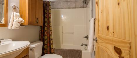 A bathroom with a toilet, sink, shower, and wooden cabinets.