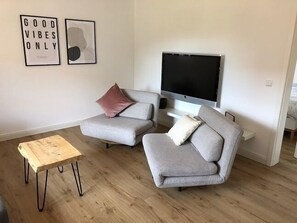Een moderne woonkamer met twee grijze banken, een houten salontafel en een flatscreen televisie aan de muur.
