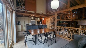 Interior espaçoso de cabana com área de refeições, cozinha e um canto acolhedor para sentar, com vista para o exterior.