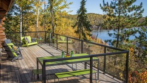 Um deck de madeira com mobiliário externo, com vista para um lago e uma floresta.
