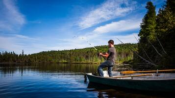 Un hombre pesca desde un bote en un lago tranquilo con una orilla boscosa.