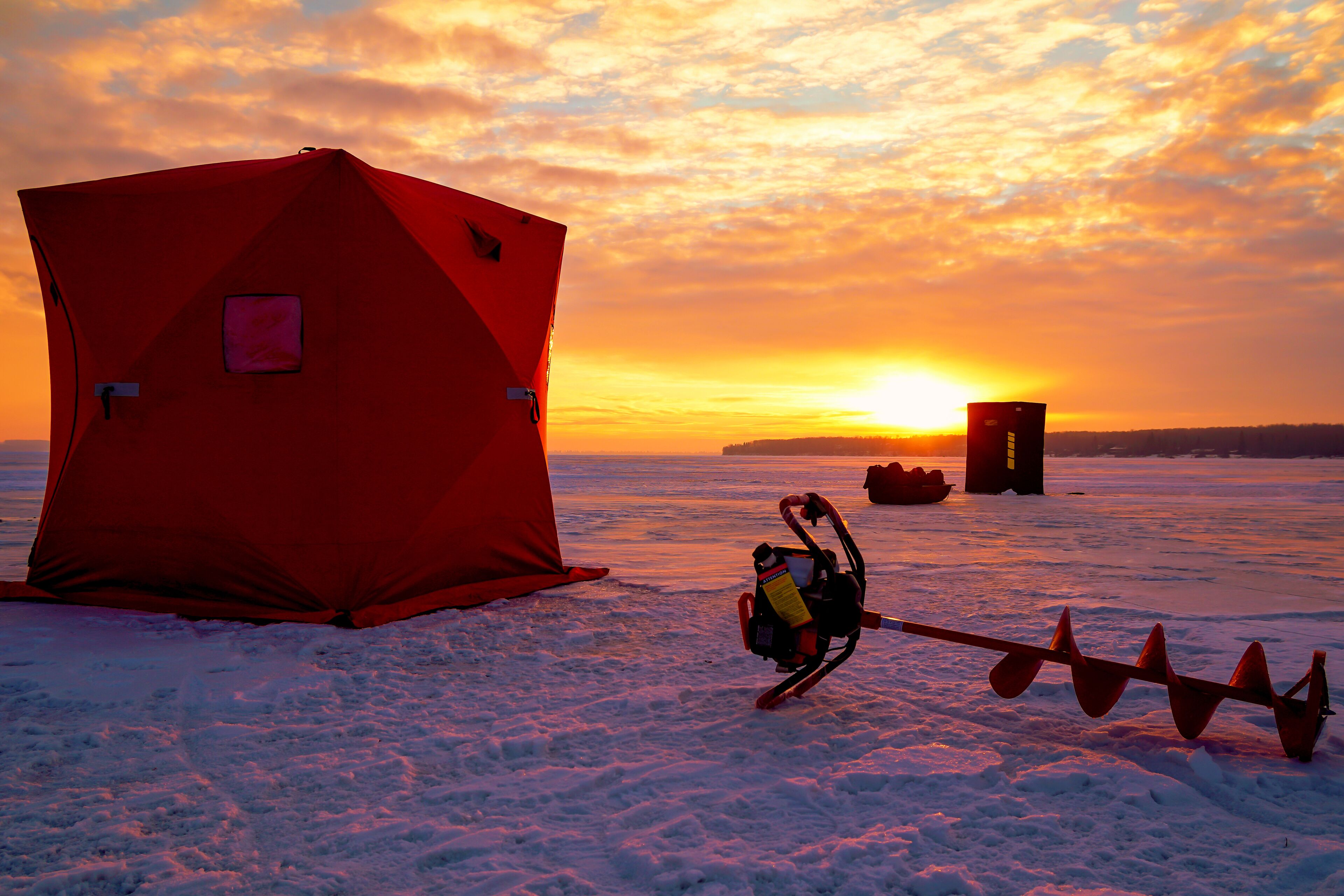 A red tent on a snowy surface with a sled and a sled puller.