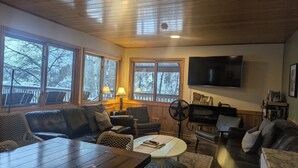 Een gezellige woonkamer met een houten plafond, grote ramen, een flatscreen televisie en comfortabele zitplaatsen.