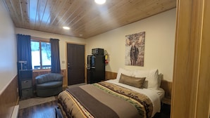 Een slaapkamer met een bed, een bureau, een stoel, een koelkast en een raam met gordijnen.