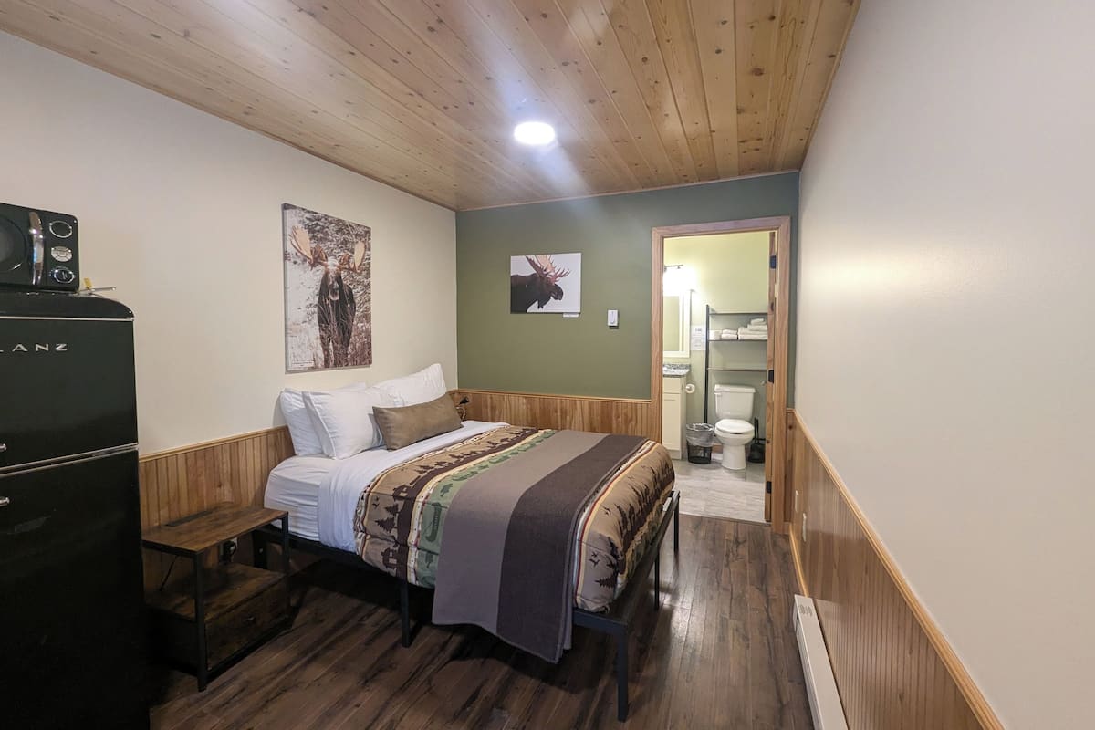 Een slaapkamer met een houten bed, een klein tafeltje, een dressoir en een deur naar de badkamer.