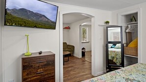 Een slaapkamer met een bed, een aan de muur bevestigde televisie, een houten dressoir en uitzicht op bergen door een raam.