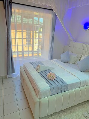 A bedroom with a large bed, a window with curtains, and a wall-mounted light fixture.