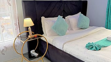 A bedroom with a bed, a bedside table with a lamp, a wall decoration, and a window with curtains.