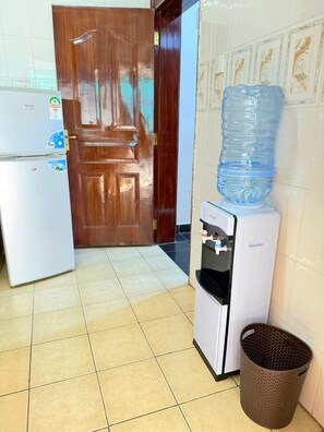 Una cocina con refrigerador, dispensador de agua, una botella grande de agua y un cubo de basura.