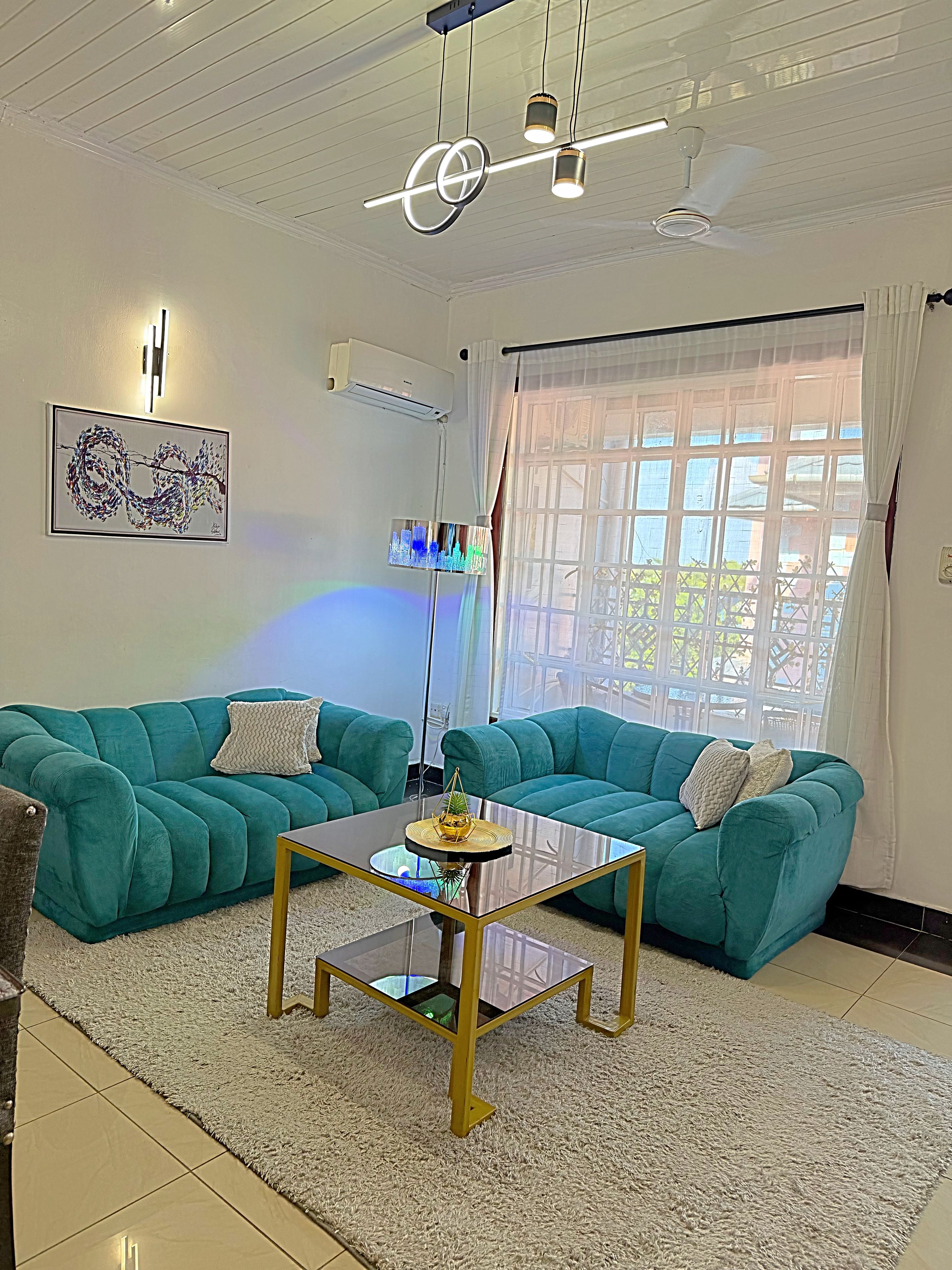 A living room with teal sofas, a glass coffee table, and a ceiling fan.