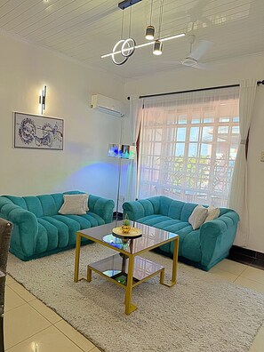 Una sala de estar con sofás color turquesa, una mesa de centro de vidrio y un ventilador de techo.