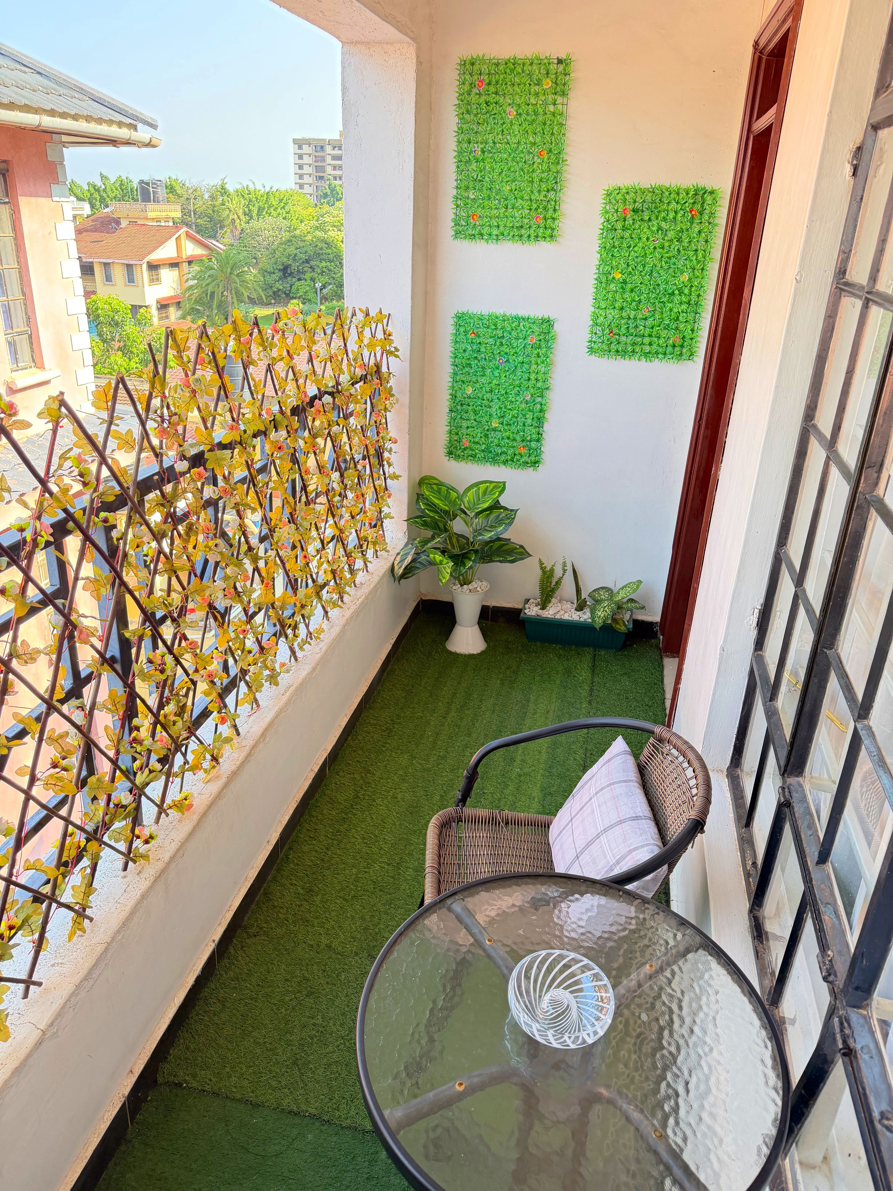 Ein Balkon mit Kunstrasen, einem Glastisch, Korbstühlen und dekorativen Wandverkleidungen.