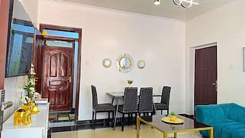 A living room with a sofa, a coffee table, a dining table with chairs, a TV, and a door.
