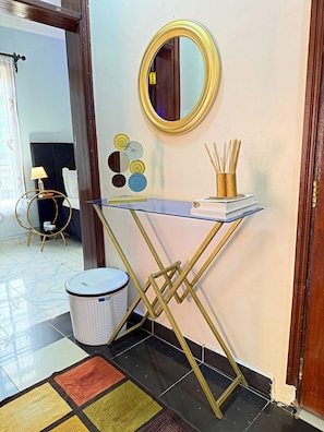 Una habitación con una mesa consola de vidrio y metal, un espejo redondo, platos decorativos y una cesta de mimbre.