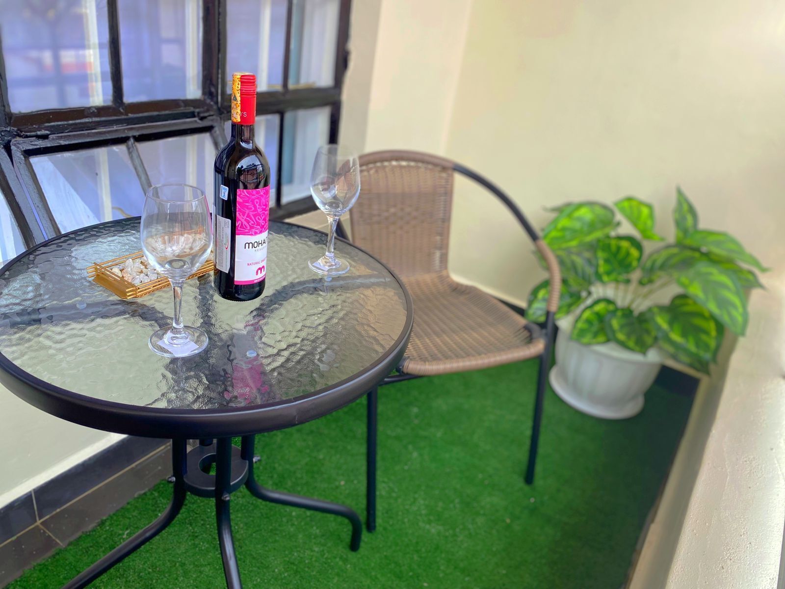 A glass table with a bottle of wine, two wine glasses, and a basket of snacks.