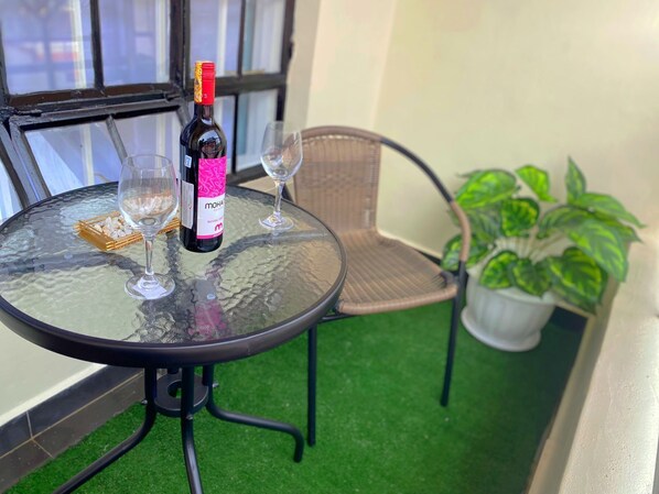 A glass table with a bottle of wine, two wine glasses, and a basket of snacks.