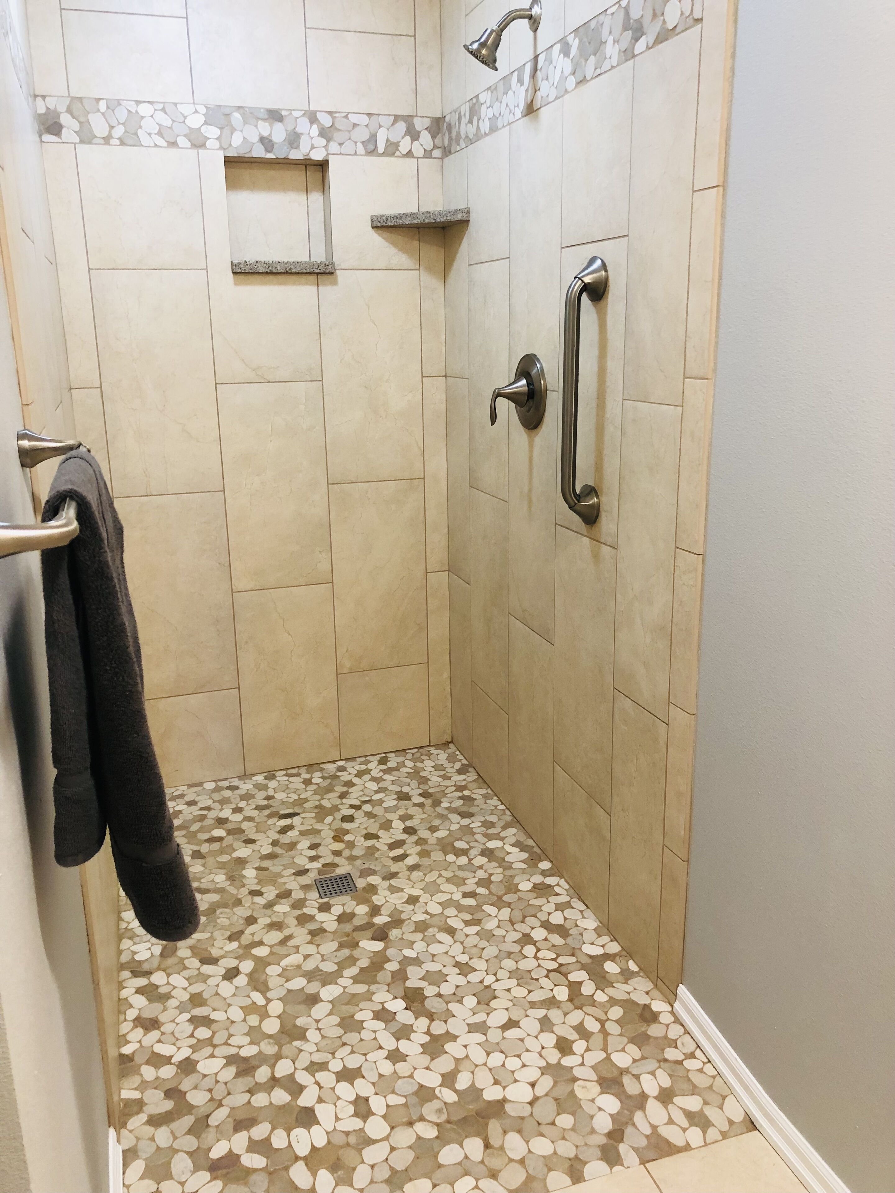 A shower with beige tiles, a pebble-patterned floor, and a towel rack.