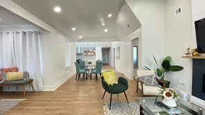 Een moderne woonkamer met een eethoek, houten vloeren en een keuken op de achtergrond.