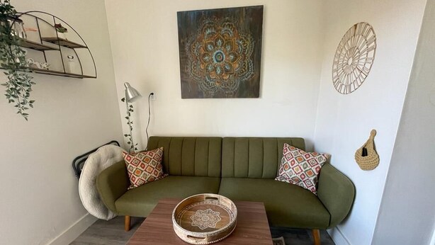 A living room with a green sofa, patterned cushions, a wooden coffee table, and decorative wall art. - Petite and Private Little Place (Lake Isabella)