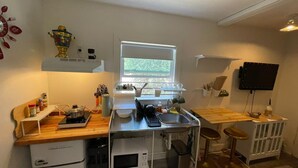 A compact kitchen with a microwave, stove, and sink. There is a window providing natural light, and a TV mounted on the wall. - Petite and Private Little Place (Lake Isabella)