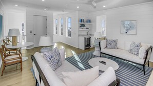 Una sala de estar moderna con un sofá blanco, una mesa de centro redonda y un comedor con una mesa y sillas blancas.