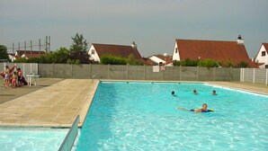 En swimmingpool med klart vand, omgivet af et hegn og huse i baggrunden.