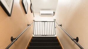 Un escalier avec une rampe, des marches recouvertes de moquette et un climatiseur fixé au mur.