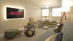 Un salon moderne avec un logo Netflix, un canapé, une table basse, une lampe et un coin repas.