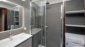 Ein modernes Badezimmer mit einer Duschkabine aus Glas, einem weißen Waschbecken und einer integrierten Waschmaschine.