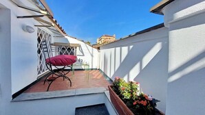 Eine kleine Terrasse im Freien mit Tisch und Stuhl, einem Blumentopf und Blick zum Himmel.