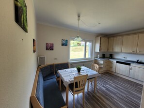 Une cuisine avec des meubles de rangement en bois, une table à manger avec des chaises, un banc intégré et une fenêtre donnant sur l’extérieur.