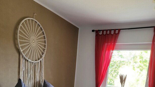 Un dormitorio moderno con una cama grande, un colgador de macramé en la pared y una ventana con cortinas rojas.
