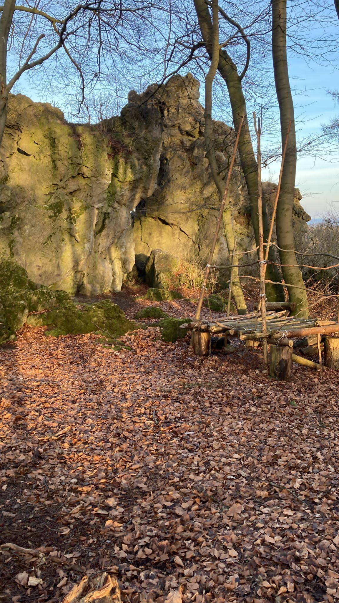 A natural rock formation with a wooden bench and trees in the foreground.