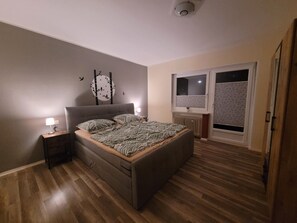 Une chambre à coucher comprenant un lit, une table de chevet, un élément de décoration murale, une fenêtre et un radiateur.