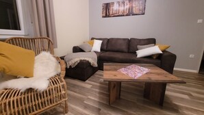 Una sala de estar con un sofá marrón, una mesa de centro de madera, un sillón de mimbre y un ventanal grande.