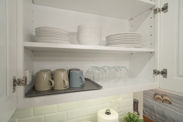 A kitchen with white cabinets, a tray with mugs and glasses, and a bed with a gray blanket.