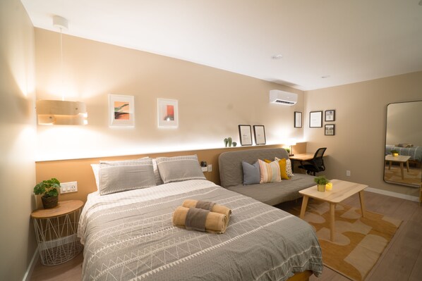 Ett modernt hotellrum med en stor säng, ett skrivbord och en stol. Det finns flera inramade tavlor på väggen och en liten växt på skrivbordet.