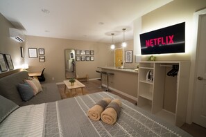 A modern hotel room with a bed, a sofa, a desk, a TV, and a wardrobe.