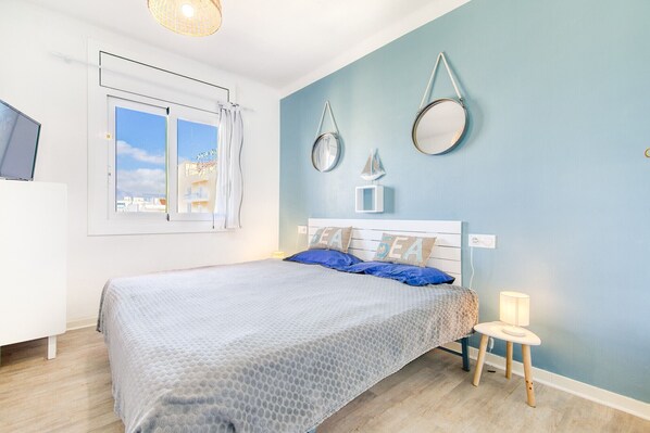 A bedroom with a bed, a bedside table, a lamp, and a window with a view of buildings.