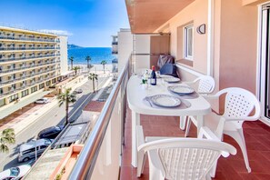 A balcony with a table set for dining, overlooking a beach and a hotel building.