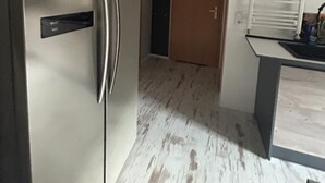 A compact kitchen with a stainless steel refrigerator, a wooden door, and a window with blinds.