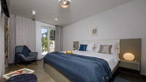 A modern hotel room with a large bed, a desk, a chair, and a view of the outdoors. - Beautiful peaceful villa with a pool in the center of Dubrovnik (Dubrovnik)