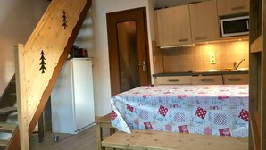 A kitchen with wooden cabinets, a microwave, and a table with a patterned tablecloth. - Arêches-Beaufort: Apt for 6-8, terrace, fully equipped, wi-fi and parking (Arêches-Beaufort)