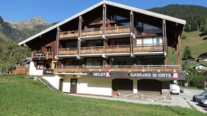 A multi-story building with balconies, a ski resort sign, and a mountain backdrop. - Arêches-Beaufort: Apt for 6-8, terrace, fully equipped, wi-fi and parking (Arêches-Beaufort)