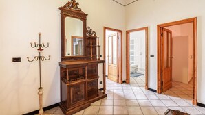Un couloir avec une grande armoire en bois, un lampadaire et un miroir. On y trouve des portes en bois et un sol carrelé.