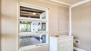 Ein Zimmer mit einem großen Fenster, einem weißen Schminktisch und einem Lüftungsgitter an der Wand.